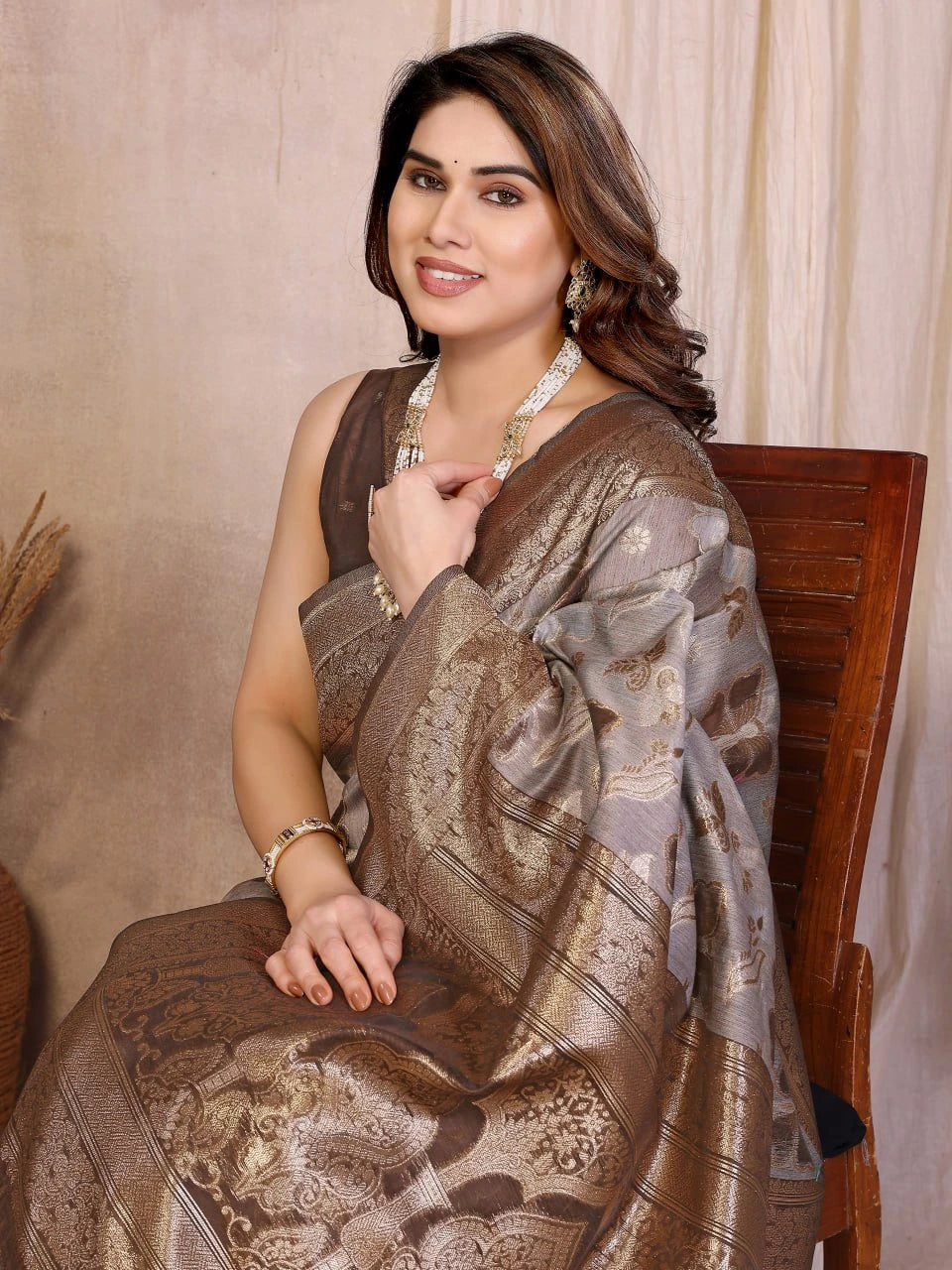 Woman wearing a patterned saree sitting on a chair against a neutral background